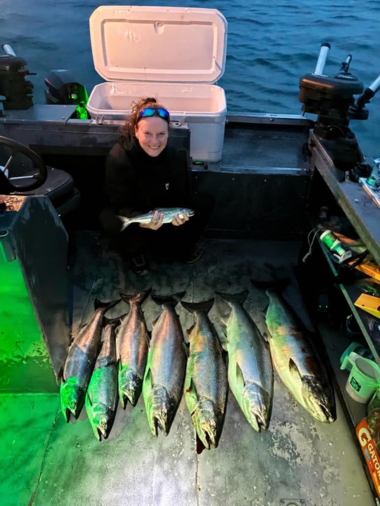 Pêcheuse souriante à bord du bateau derrière une rangée de saumons alignés sur le pont