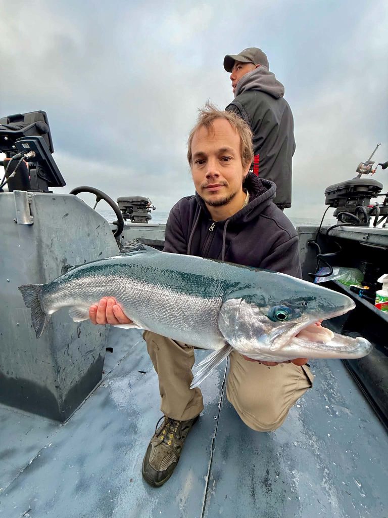 Jeune pêcheur à bord du bateau tenant un saumon coho aux reflets argentés