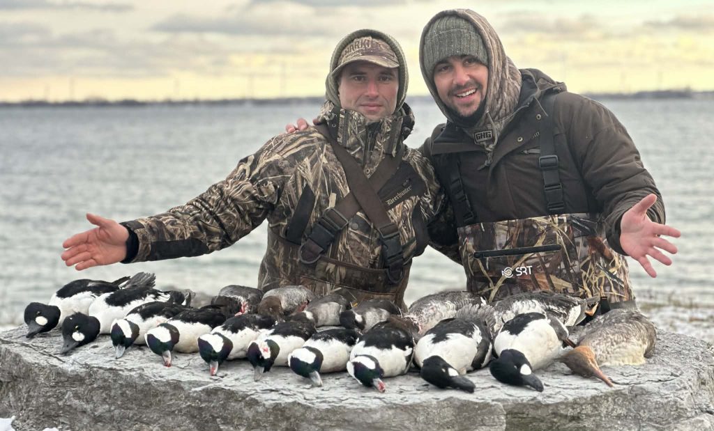 Deux chasseurs souriants sur le roc derrière une rangée de garrots et de petits garrots, le lac en arrière-plan