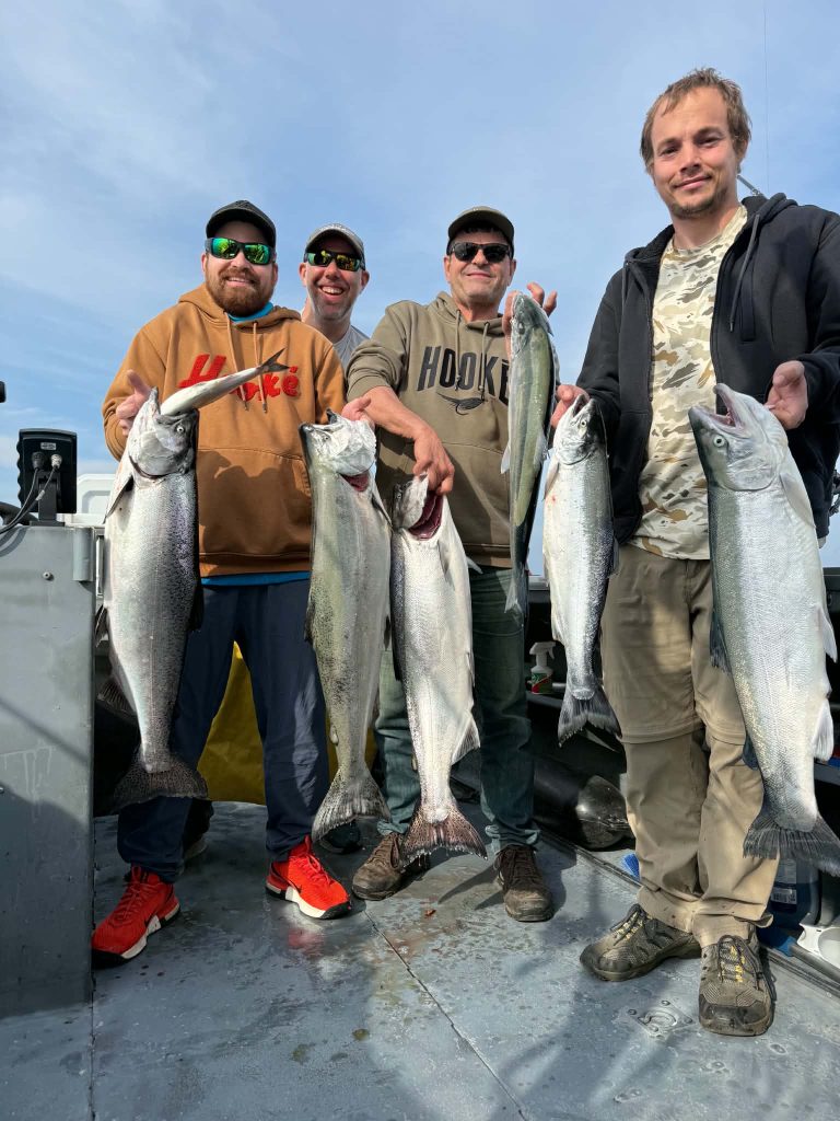 Quatre pêcheurs souriants à bord du bateau, chacun tenant ses saumons