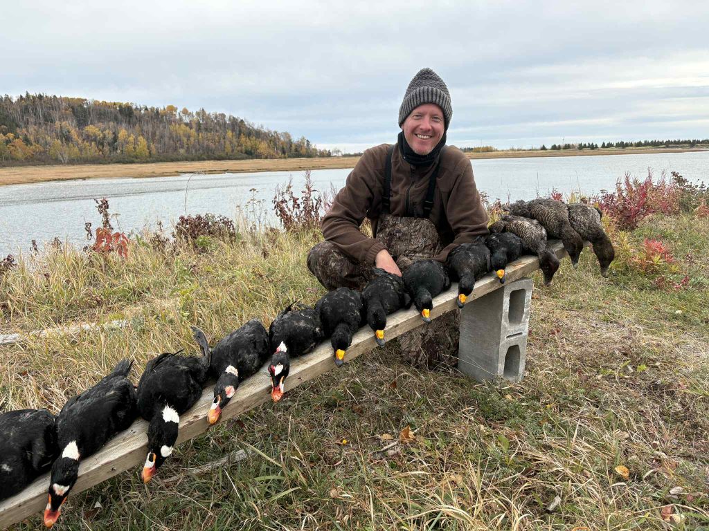 Chasseur souriant derrière une longue rangée de macreuses alignées au bord de l’eau en automne