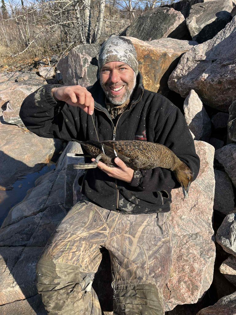 Chasseur souriant sur les rochers tenant un canard de mer portant une bague de recherche