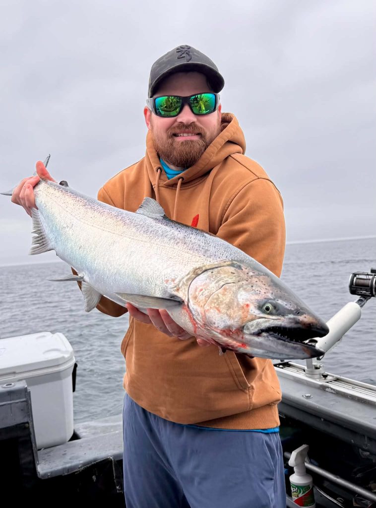 Pêcheur portant des lunettes de soleil, tenant un gros saumon chinook à bord du bateau