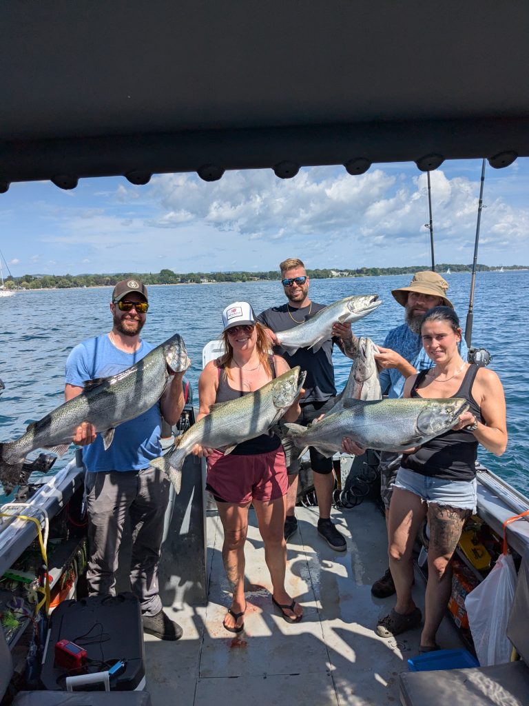 Groupe de six pêcheurs à bord du bateau brandissant leurs saumons par une belle journée d’été