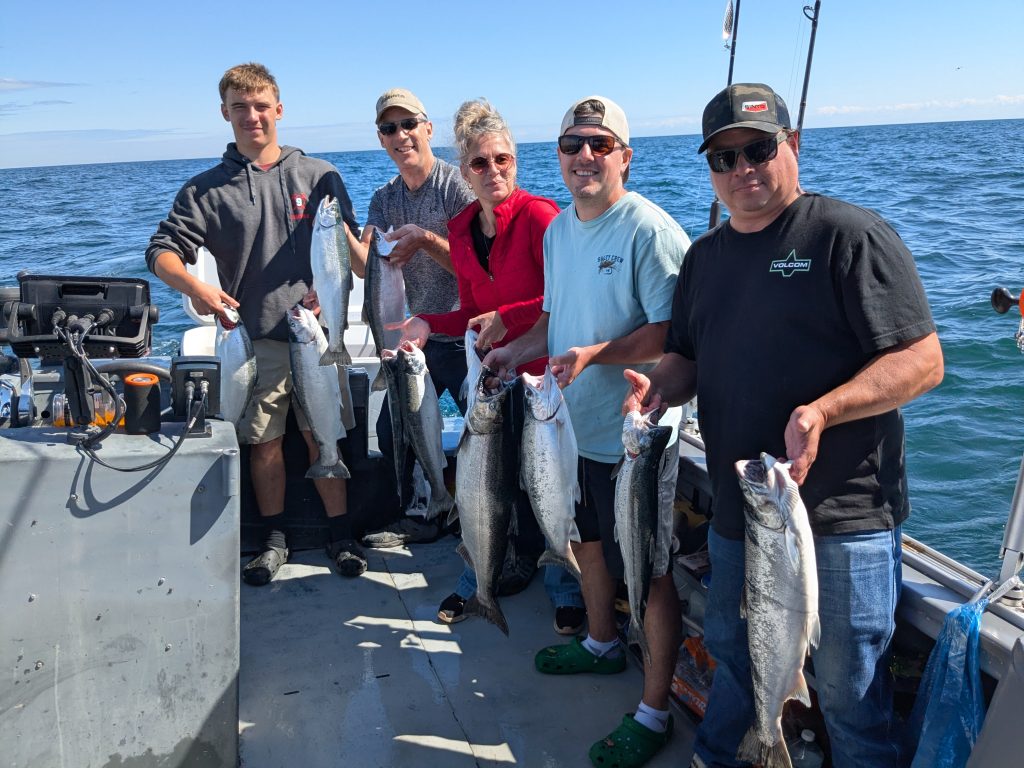 Six pêcheurs alignés à bord du bateau, chacun tenant ses saumons et truites