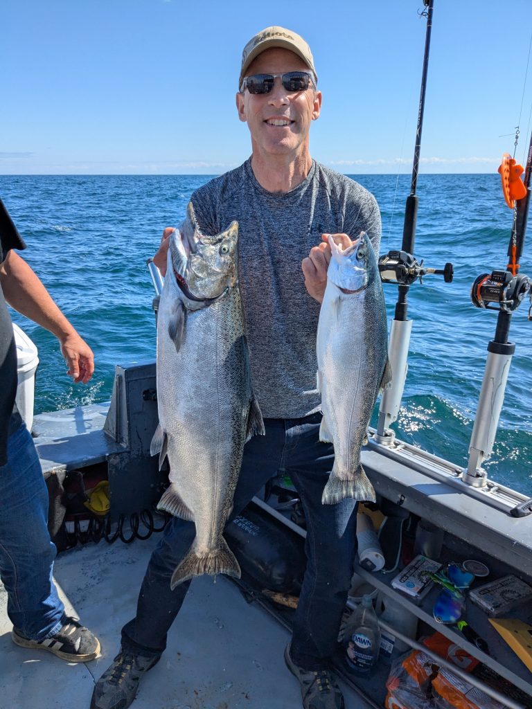 Pêcheur à bord du bateau tenant un saumon dans une main et une truite arc-en-ciel dans l’autre