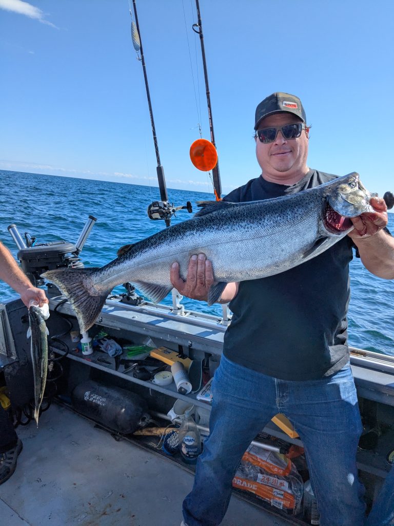 Pêcheur souriant à bord du bateau tenant un saumon chinook à deux mains