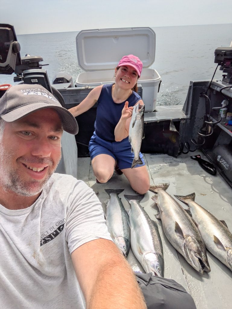 Selfie du guide et d’une pêcheuse à bord du bateau, avec les saumons de la journée alignés sur le pont