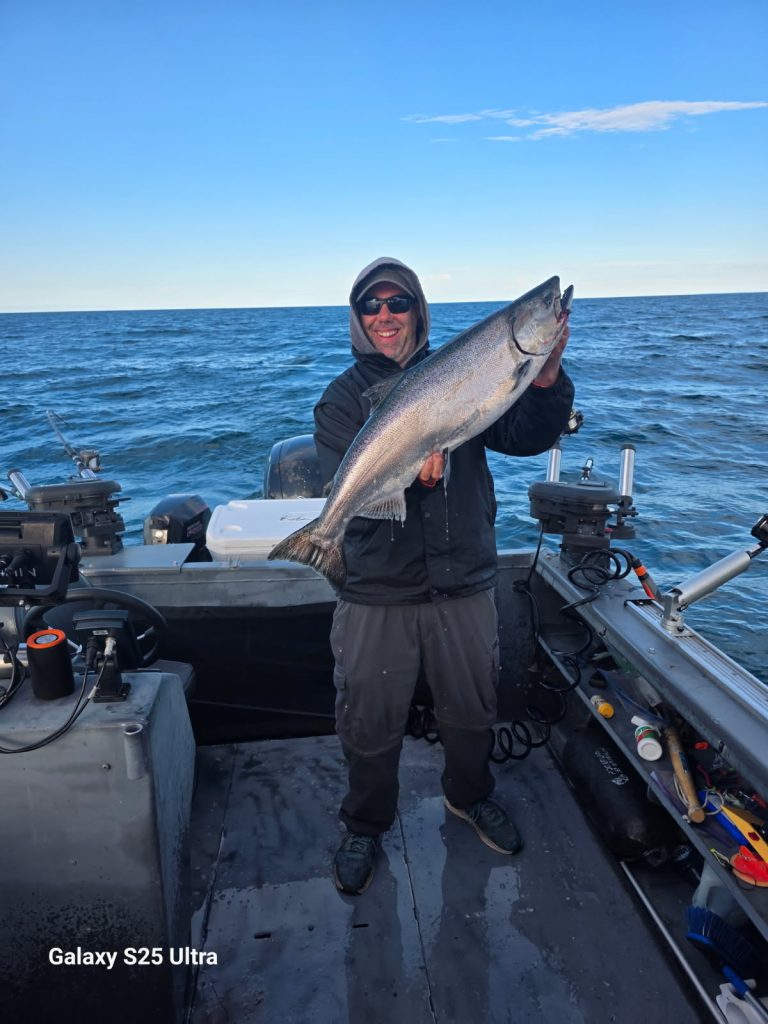 Pêcheur à bord du bateau tenant un gros saumon chinook, le lac Ontario en arrière-plan