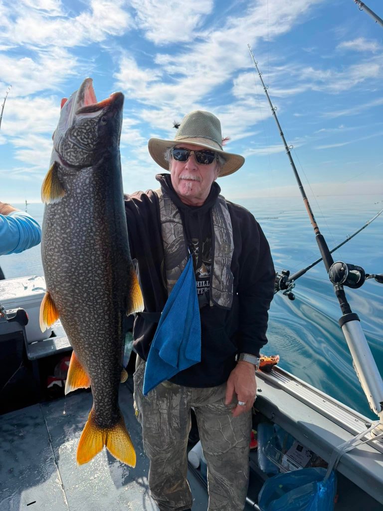 Pêcheur à bord du bateau tenant une grosse truite grise aux nageoires orangées