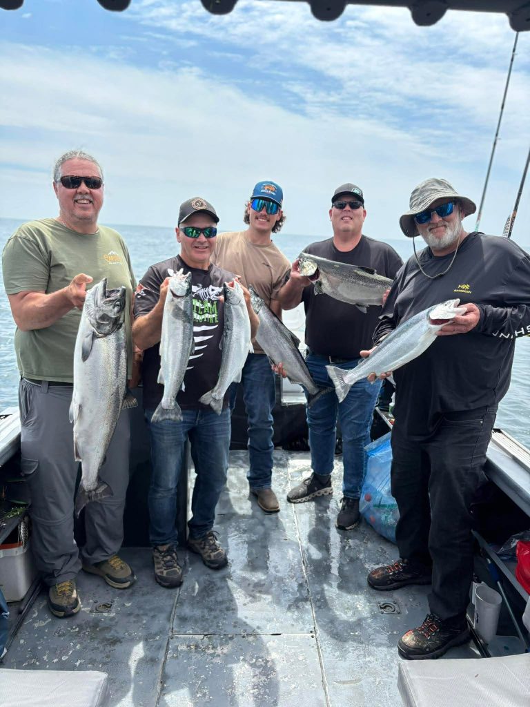 Six pêcheurs alignés à bord du bateau, chacun tenant les saumons de la journée