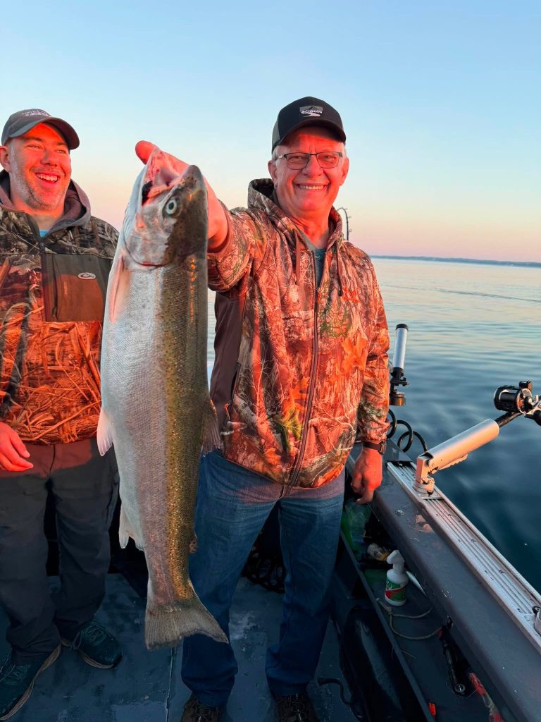 Deux pêcheurs à bord du bateau, l’un tenant une truite arc-en-ciel, au coucher du soleil