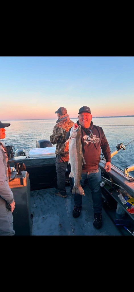 Pêcheur à bord du bateau tenant une truite, au coucher du soleil sur le lac
